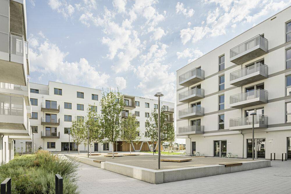 Moderne Wohnanlage mit weißen Fassaden, Balkonen und einem begrünten Innenhof unter blauem Himmel.