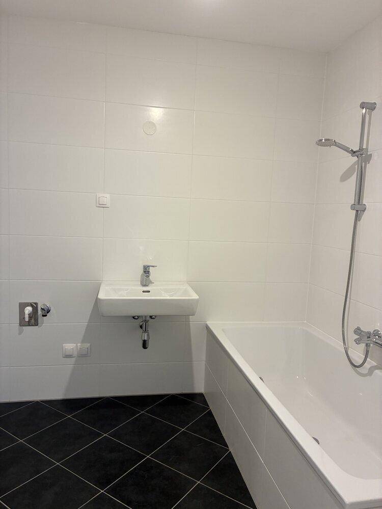 Modernes Badezimmer mit weißen Wandfliesen, schwarzem Boden und Badewanne mit Duschfunktion.