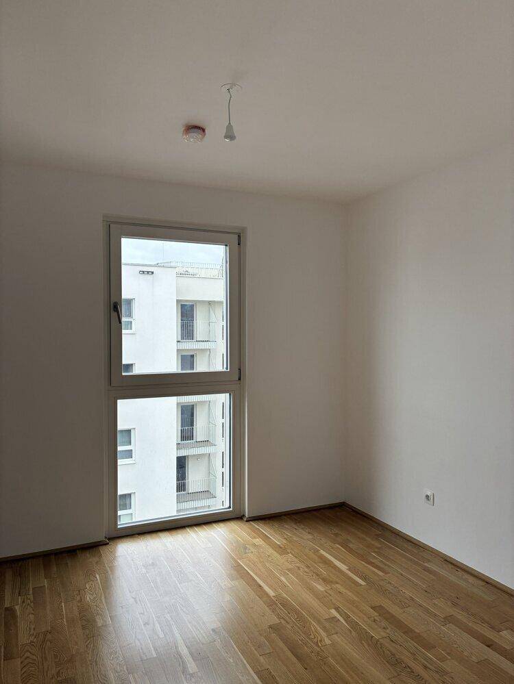 Helles Schlafzimmer mit Parkettboden und Blick auf die umliegenden Gebäude.