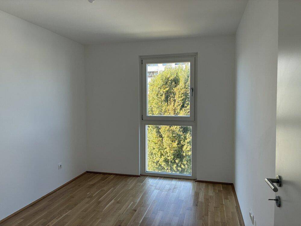 Ruhiges Schlafzimmer mit Parkettboden und Fenster, das einen grünen Baumblick bietet.
