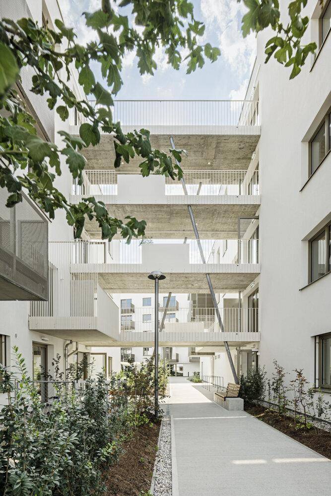 Moderner Gebäudekomplex mit offenen Laubengängen und begrünten Wegen zwischen den Wohneinheiten.