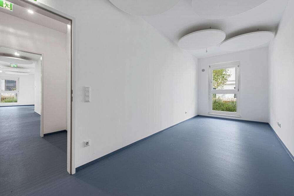Geräumiger, heller Raum mit blauer Bodenfläche, weißen Wänden und einem Fenster.