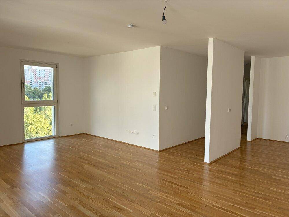 Geräumiges, helles Zimmer mit Holzboden und Blick auf die Stadt und Bäume.