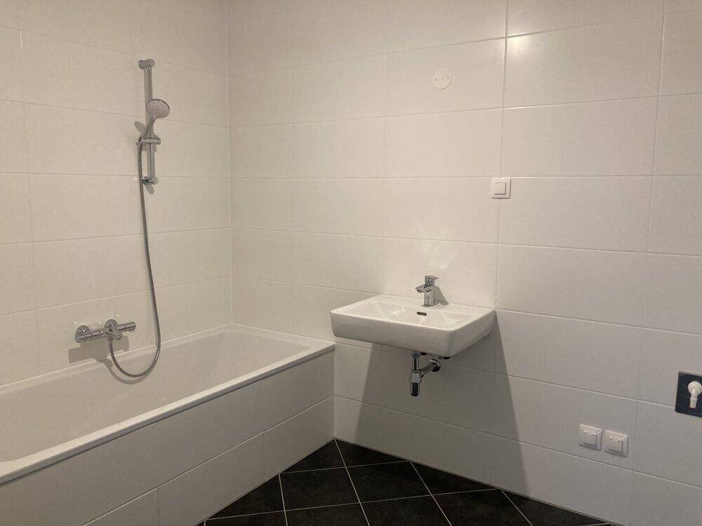 Modernes Badezimmer mit Badewanne, Waschbecken und weißen Fliesen an den Wänden sowie dunklem Boden.