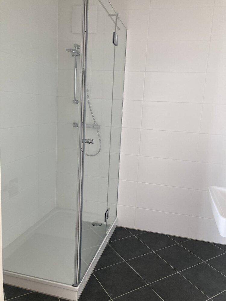 Modernes Badezimmer mit Duschkabine und dunklen Fliesen, ausgestattet mit einer Glasabtrennung.