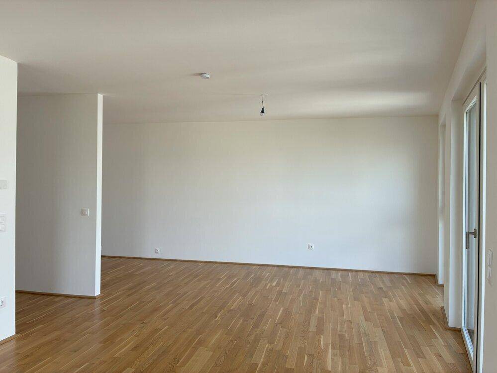 Weitläufiger, heller Raum mit Holzboden und Zugang zu einem Balkon oder einer Terrasse.