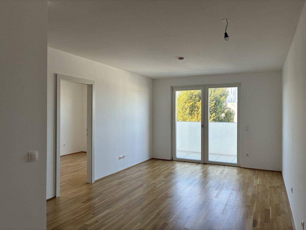 Heller Wohnraum mit Parkettboden und Zugang zu einem Balkon oder einer Terrasse.