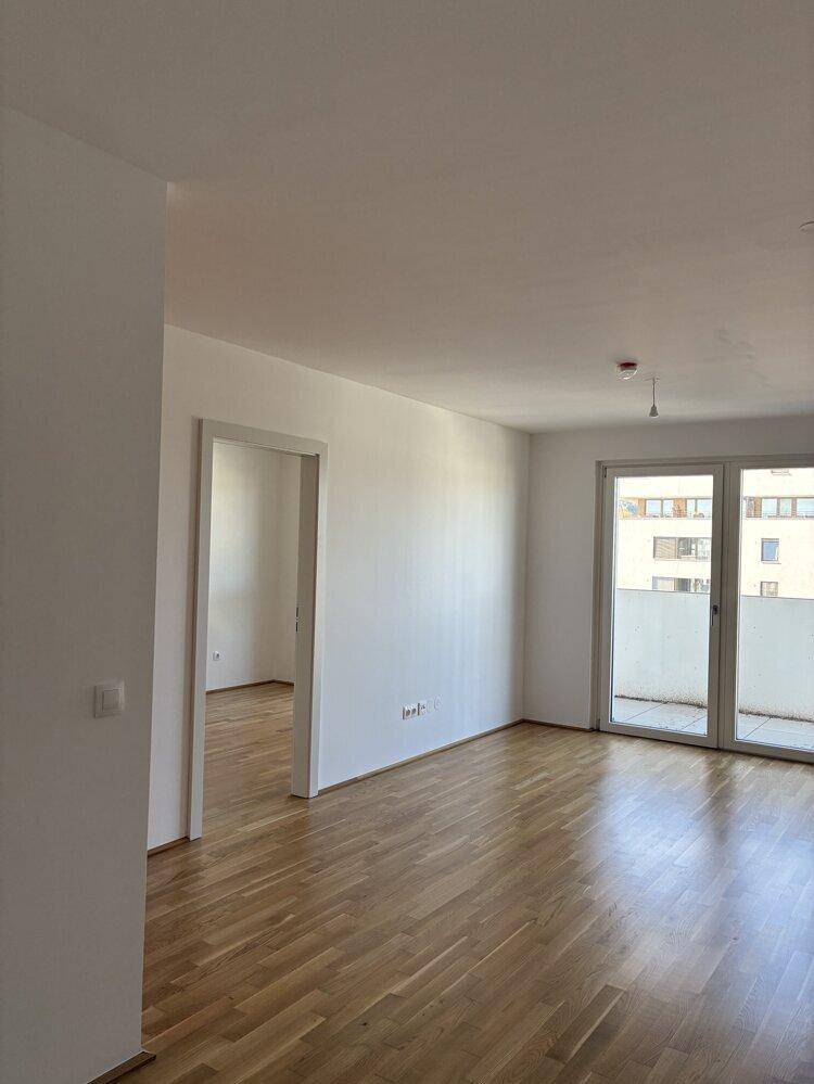 Geräumiger Wohnbereich mit Parkettboden und großen Fenstern, die viel Tageslicht hereinlassen.