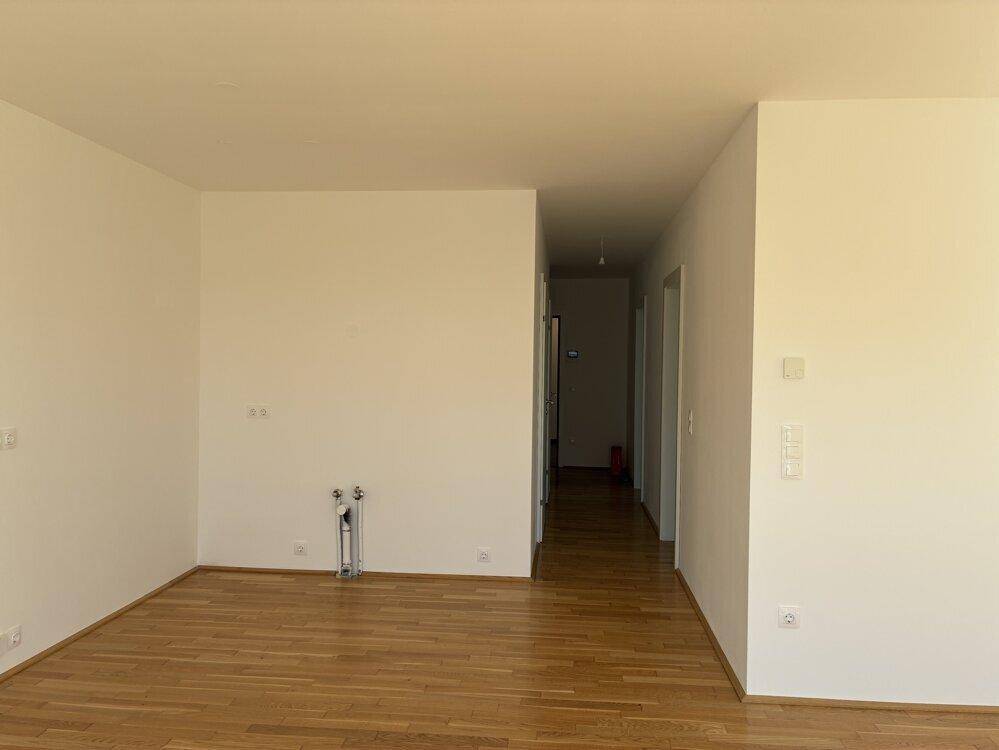 Heller Wohnbereich mit Parkettboden und Anschlüssen für eine zukünftige Küche.