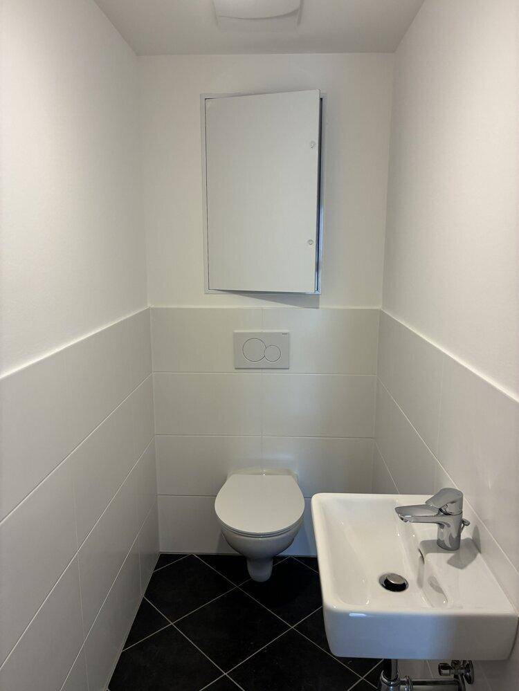 Modernes Gäste-WC mit Wand-WC, kleinem Waschbecken und weißen Fliesen an den Wänden.