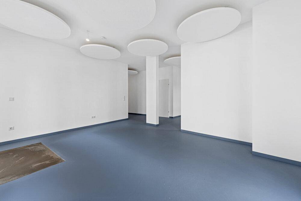 Geräumiger, heller Innenraum mit weißen Wänden, blauem Boden und modernen Deckenelementen.