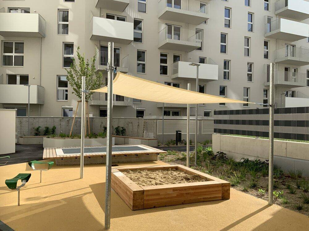 Kinderspielplatz im Innenhof mit Sandkasten, Sonnensegel und Sitzgelegenheiten für Kinder.