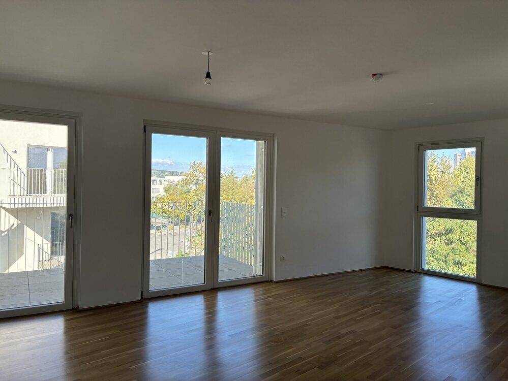 Geräumiges Wohnzimmer mit Holzboden und Zugang zu einem Balkon, bietet viel Tageslicht.