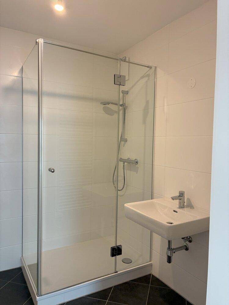 Modernes Badezimmer mit Duschkabine, weißen Fliesen und dunklem Boden.