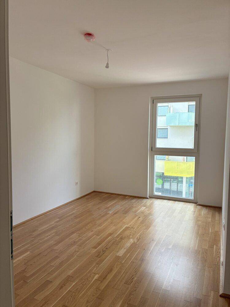 Helles Schlafzimmer mit Parkettboden und großem Fenster, das eine angenehme Atmosphäre schafft.