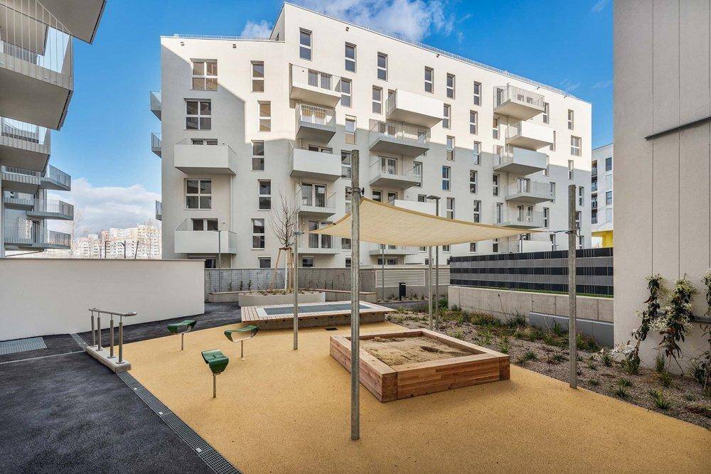 Kinderspielplatz mit Sandkästen und Sonnensegel im Innenhof eines modernen Wohnkomplexes.