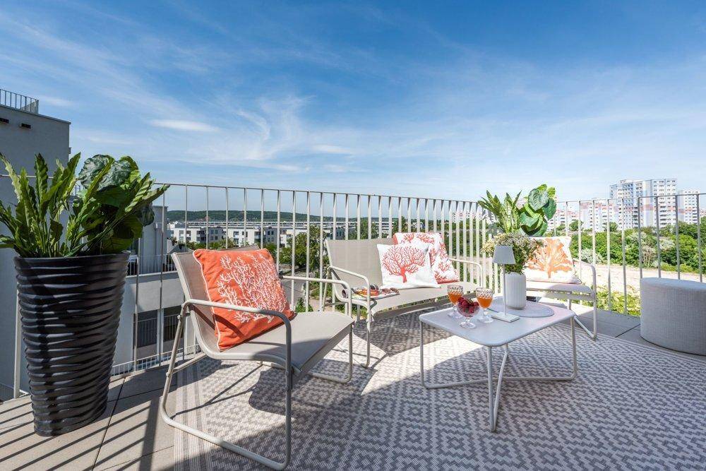 Geräumiger Balkon mit modernen Gartenmöbeln und weitem Blick über die Stadtlandschaft unter blauem Himmel.