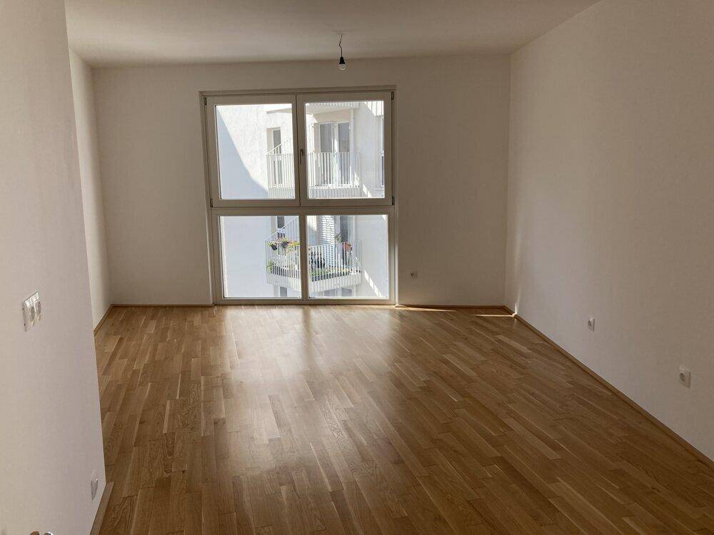 Helles, leeres Zimmer mit großen Fenstern und Parkettboden, bereit zur individuellen Gestaltung.
