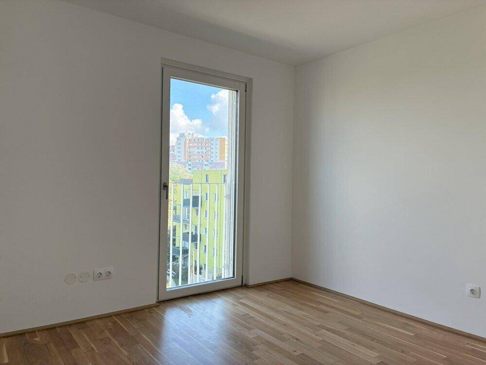 Helles Zimmer mit Holzboden und einem französischen Balkon, bietet einen Blick auf die Umgebung.