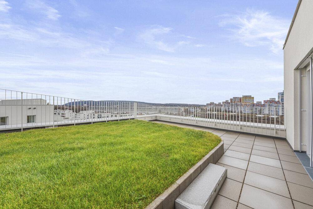 Weitläufige Dachterrasse mit Grünfläche und Fliesen, die einen beeindruckenden Panoramablick über die Stadt bietet.