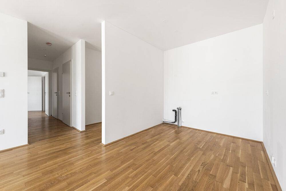 Leerer Raum mit Holzboden und Zugang zu einem Flur, bereit für die individuelle Gestaltung.