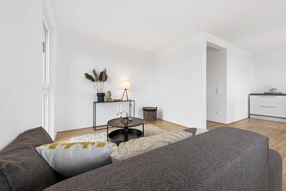 Heller Wohnbereich mit bequemer Couch, modernem Beistelltisch und Blick in die angrenzende Küche.