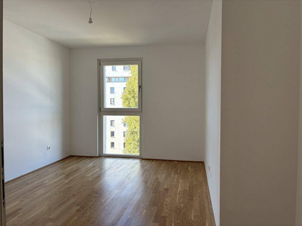 Geräumiges Schlafzimmer mit Holzboden und großem Fenster, ideal für natürliche Beleuchtung.