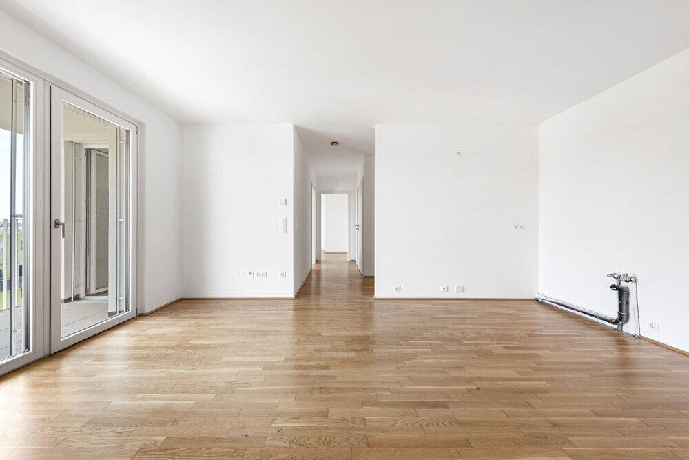 Geräumiger, heller Raum mit Parkettboden, Küchenanschlüssen und Zugang zu einem Balkon.