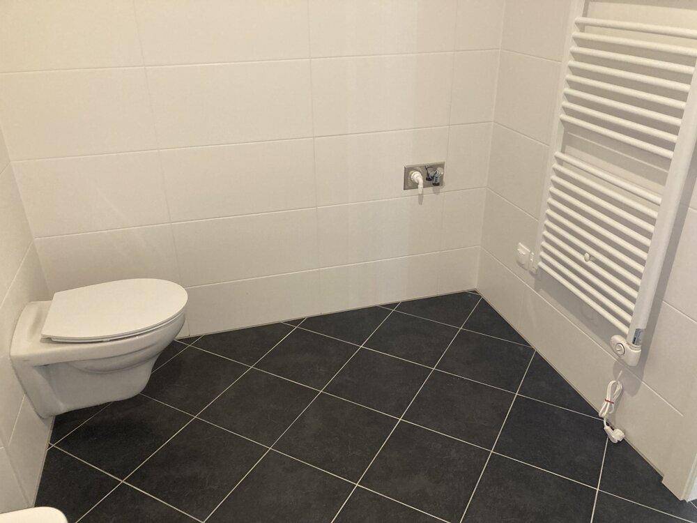 Modernes WC mit Wand-WC, dunklen Fliesen und beheiztem Handtuchhalter.