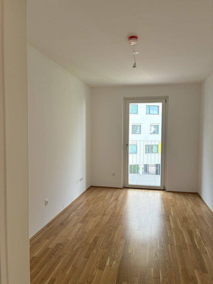 Ruhiges Schlafzimmer mit Parkettboden und Fenster, das viel Tageslicht hereinlässt.