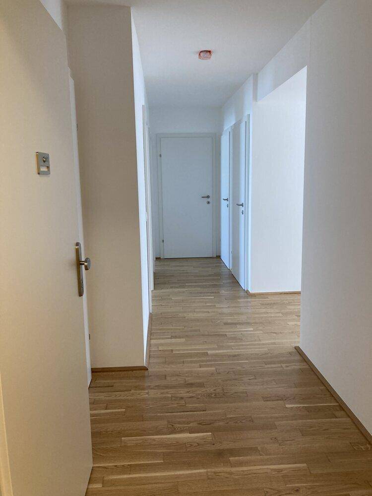 Langer, heller Flur mit Parkettboden und mehreren weißen Türen in einem modernen Gebäude.
