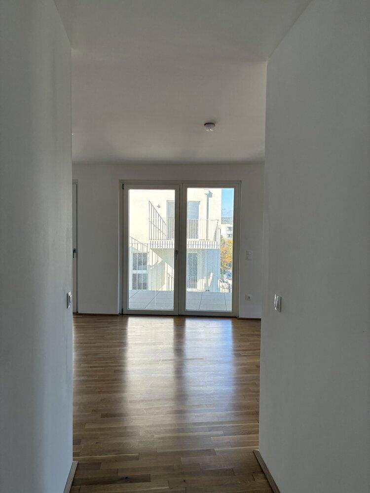 Flur mit Parkettboden und Blick auf die großen Balkontüren, die viel Licht hereinlassen.