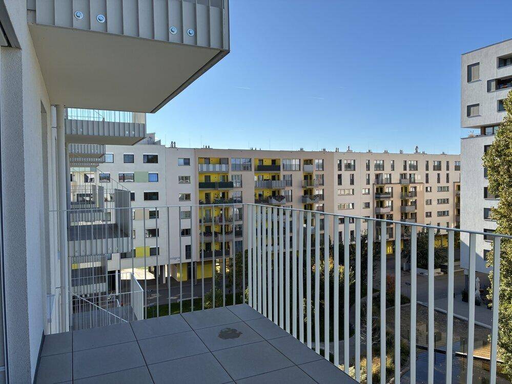 Balkon mit Blick auf den begrünten Innenhof und die umliegenden modernen Gebäude.