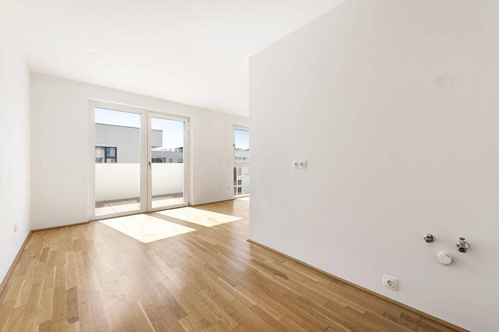 Heller Raum mit Holzboden und Balkonzugang, vorbereitet für eine Küche.