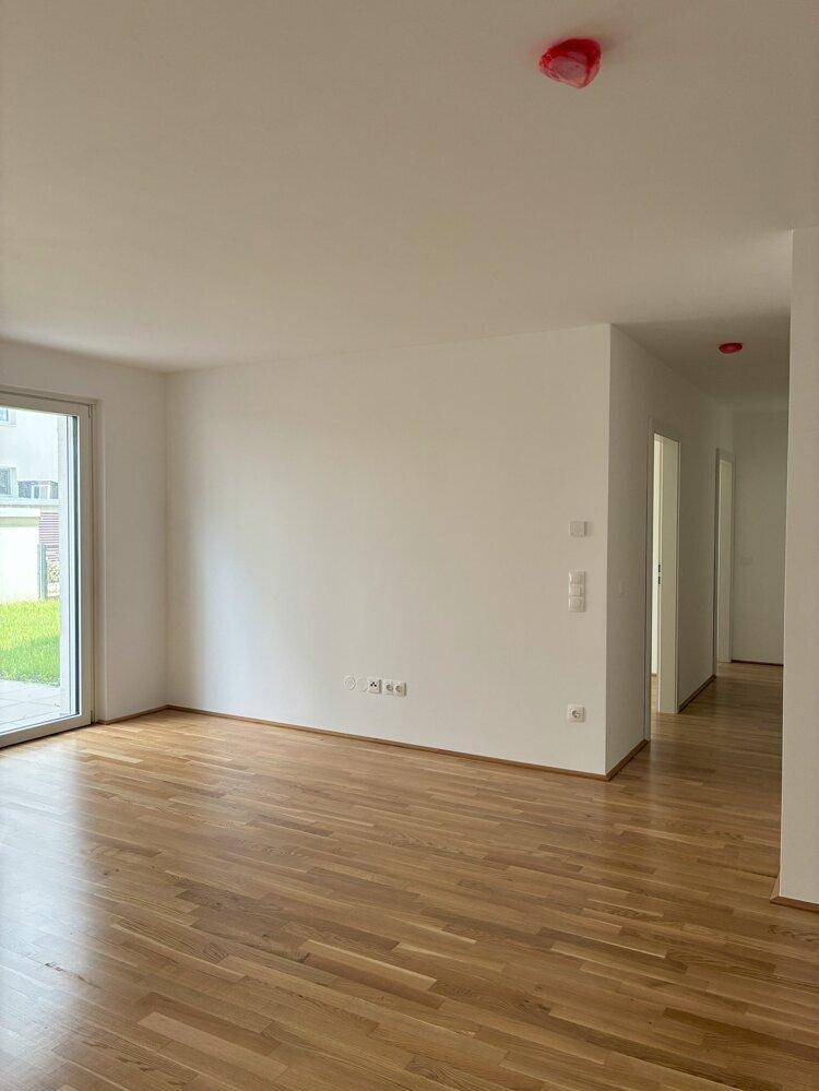 Heller, leerer Wohnraum mit Holzboden und Zugang zu einem Außenbereich, bereit zur Einrichtung.