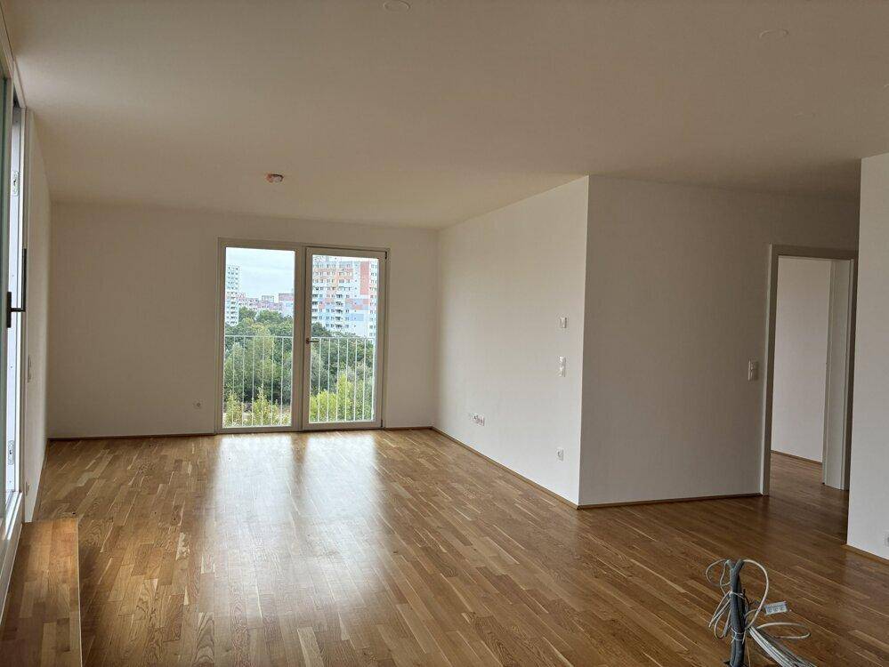 Helles Wohnzimmer mit Parkettboden, weißen Wänden und Fenstern mit Blick ins Grüne und auf die Stadt.