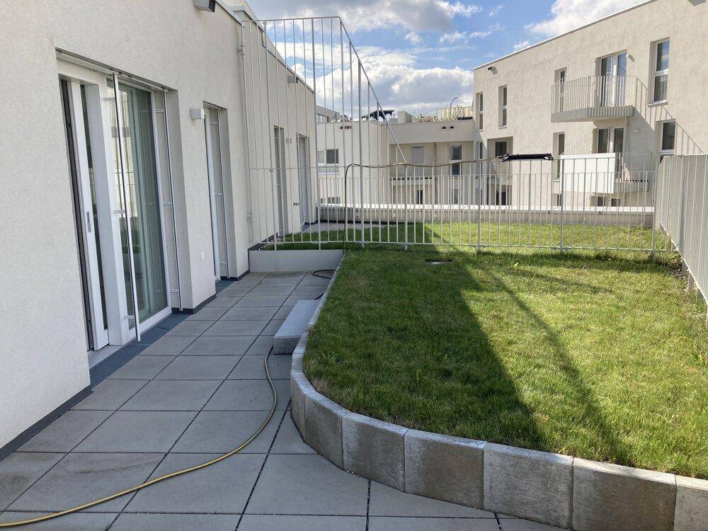 Sonniger Terrassenbereich mit Fliesen und kleiner Rasenfläche, direkt am Gebäude gelegen.