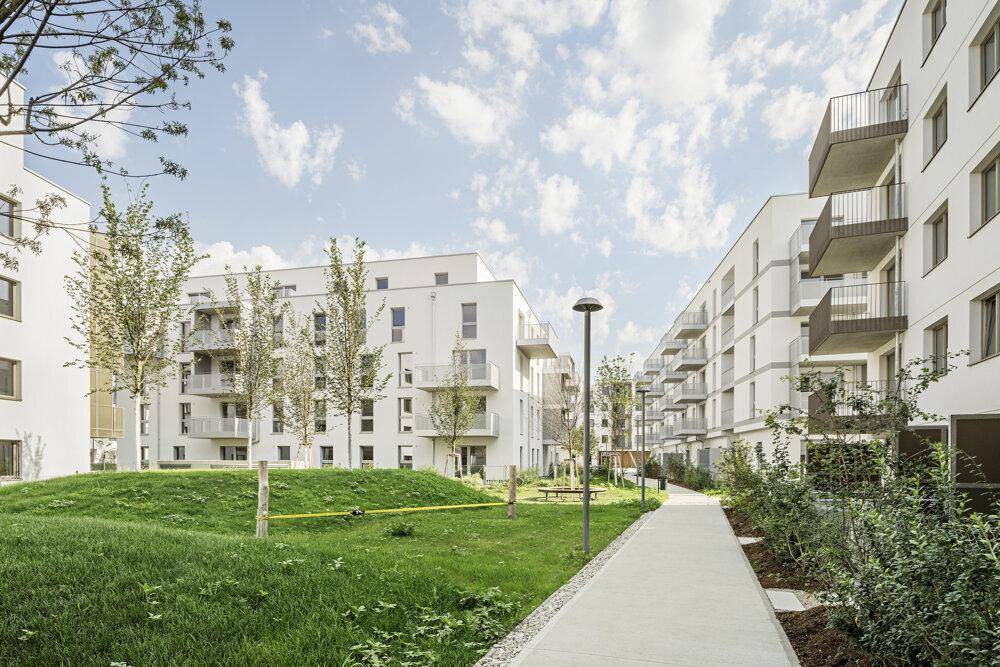 Weitläufige moderne Wohnanlage mit Grünflächen, Bäumen und Wegen zwischen den Gebäuden.
