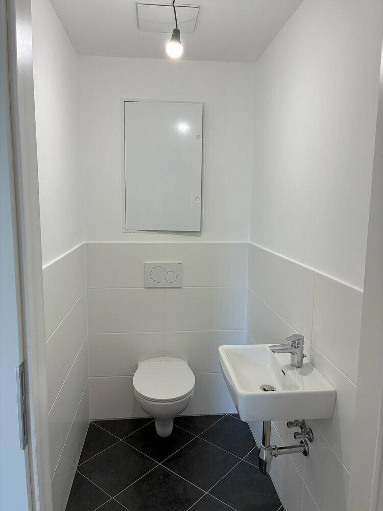 Kleines Gäste-WC mit Wand-WC, Waschbecken und dunklen Bodenfliesen in modernem Design.