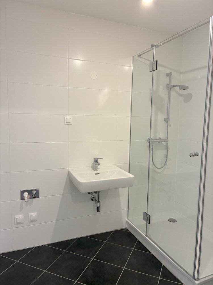 Modernes Badezimmer mit weißen Wandfliesen, schwarzem Boden und einer geräumigen Duschkabine.