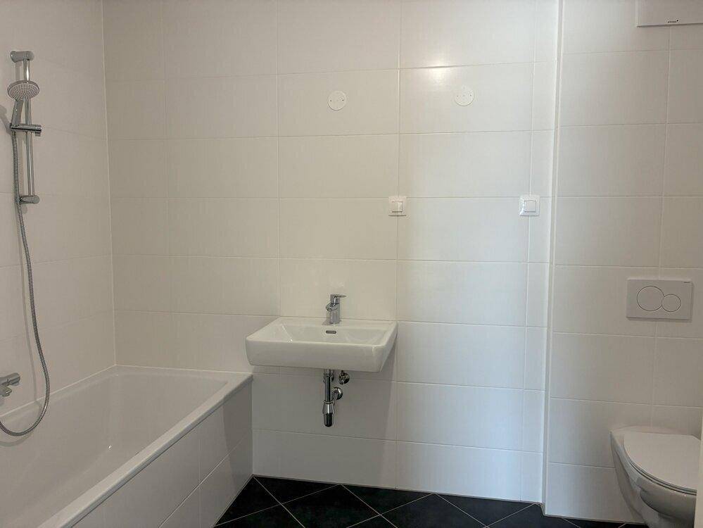 Modernes Badezimmer mit weißen Fliesen, Badewanne mit Duschfunktion, Waschbecken und WC.