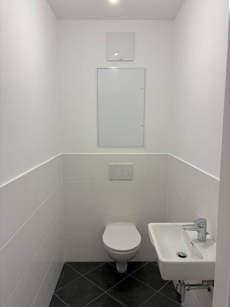Modernes Gäste-WC mit weißen Fliesen, wandhängendem WC und kleinem Waschbecken.