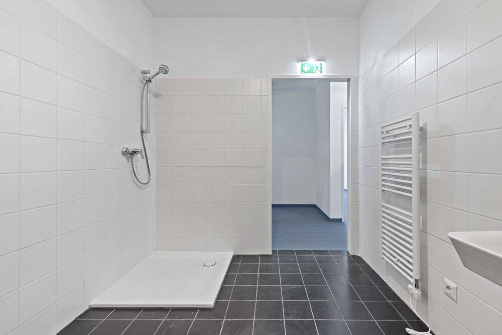 Modernes Badezimmer mit weißen Fliesen, dunklem Boden und einer ebenerdigen Dusche.