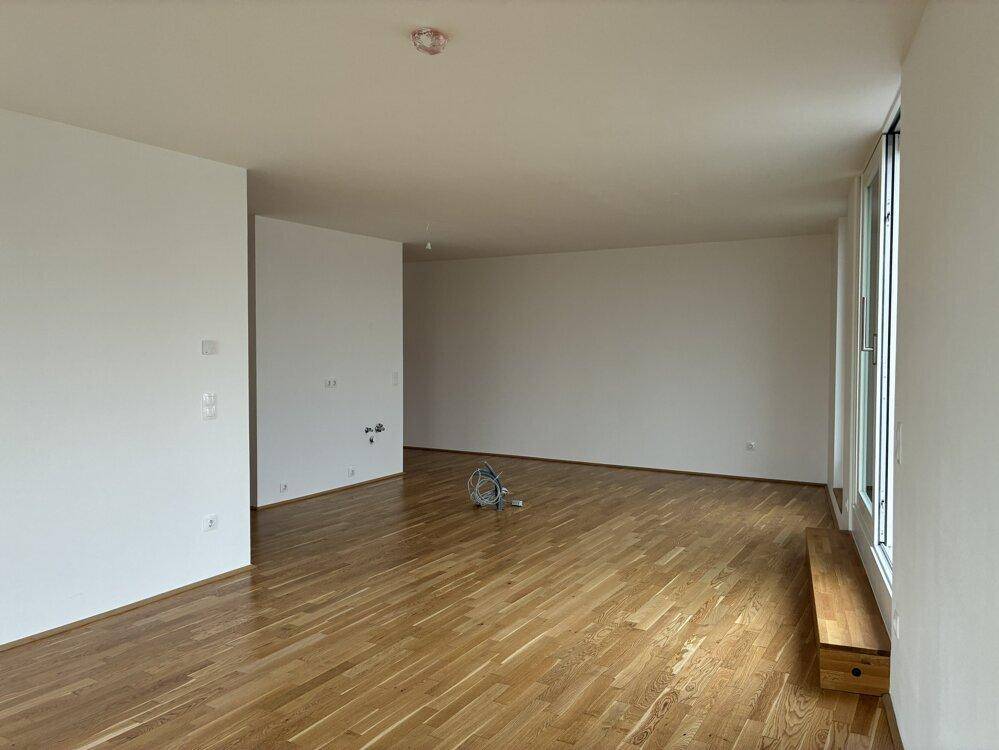 Großzügiges Wohnzimmer mit Parkettboden, weißen Wänden und viel natürlichem Licht durch große Fenster.