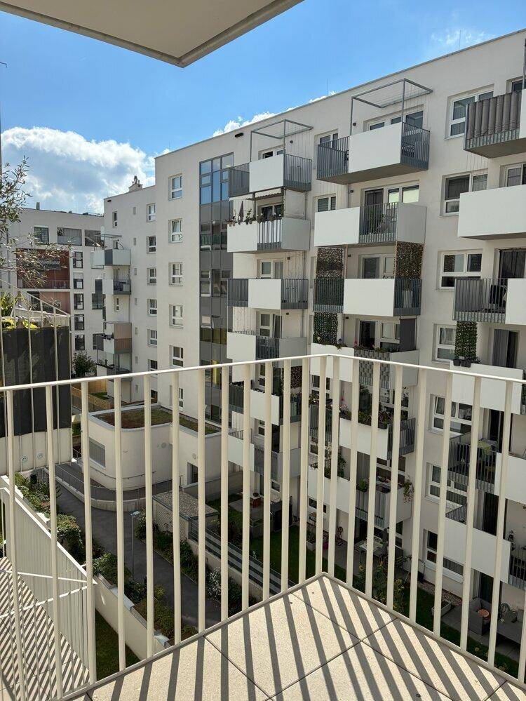 Blick vom Balkon auf den begrünten Innenhof und die modernen Wohngebäude der Anlage.