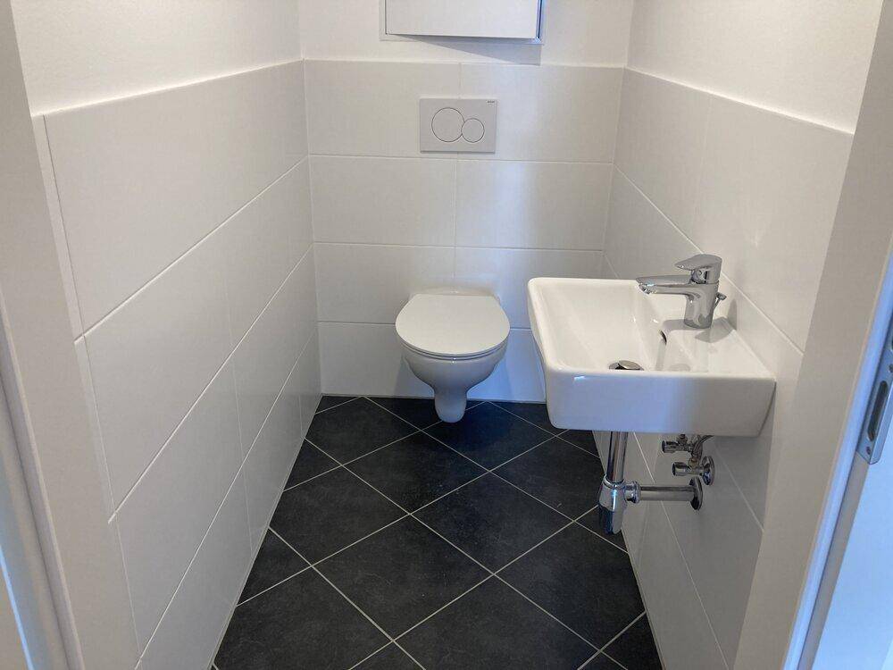 Separates Gäste-WC mit wandhängender Toilette, kleinem Waschbecken und modernen dunklen Bodenfliesen.