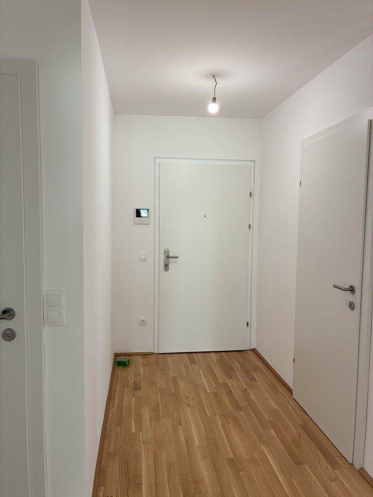 Eingangsbereich der Wohnung mit Holzboden, weißer Tür und Gegensprechanlage, hell und einladend.