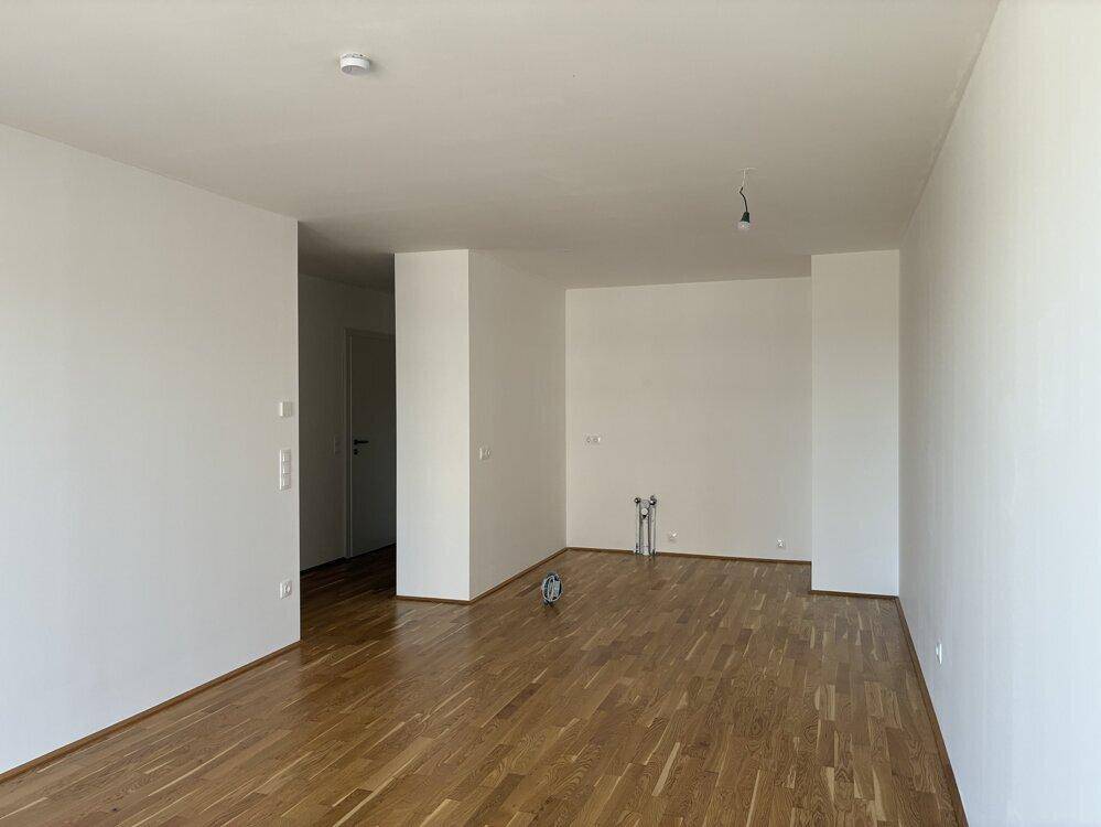 Geräumiger, heller Raum mit Holzboden und Anschlüssen für eine zukünftige Küche.