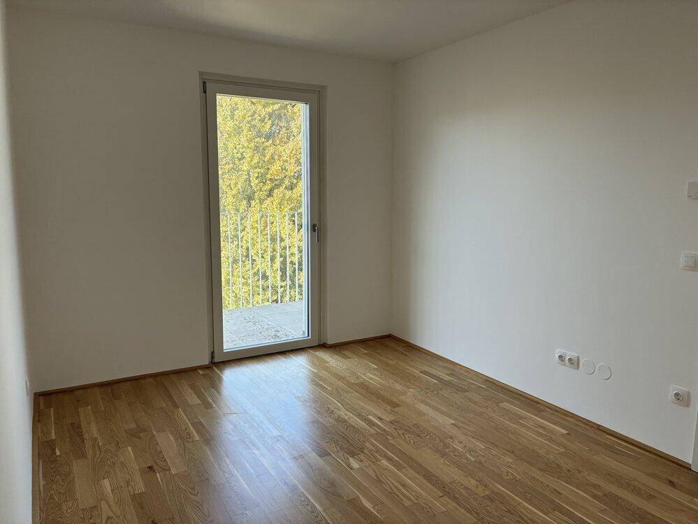 Ruhiges Schlafzimmer mit Parkettboden und Balkonzugang, umgeben von grünen Bäumen.