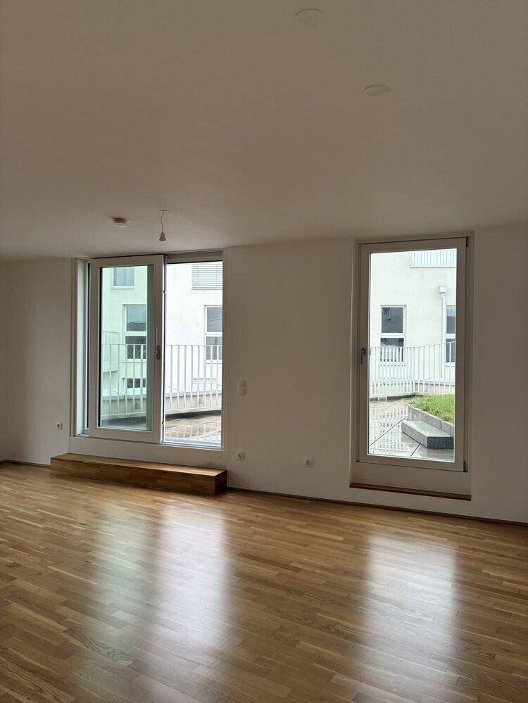 Modernes Wohnzimmer mit Parkettboden und großen Fenstern, die den Raum erhellen.